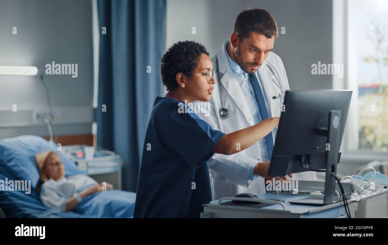 Krankenhausabteilung: Kaukasischer Arzt Spricht Mit Professioneller Schwarzkopfkrankenschwester, Sie Verwenden High-Tech-Computer. Im Hintergrund Patient im Bett erholt sich nach Stockfoto