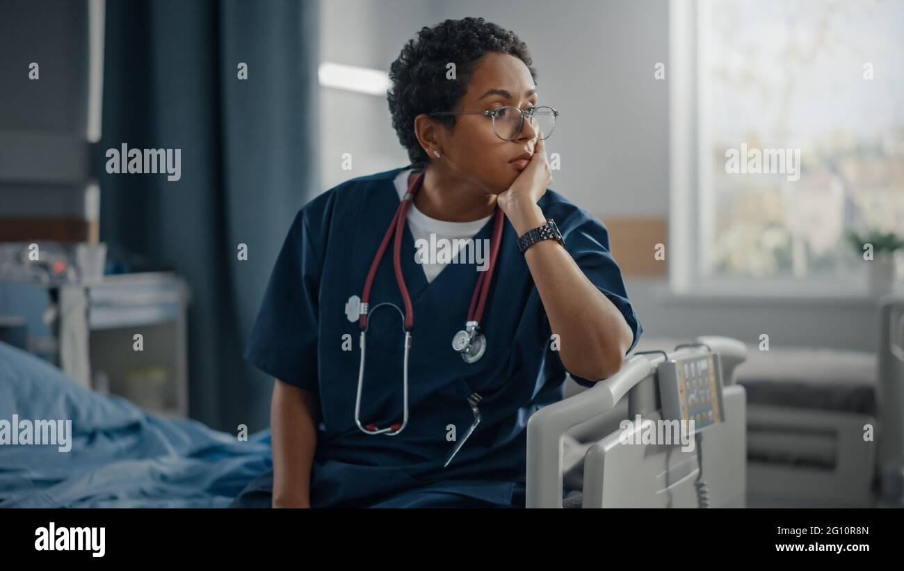 Krankenstation: Porträt einer trauernden, schwarzen Krankenschwester, die auf einem Bett sitzt und ihren Kopf in Trauer für alle Patienten hält, die bei der Pandemie nicht gerettet werden konnten Stockfoto