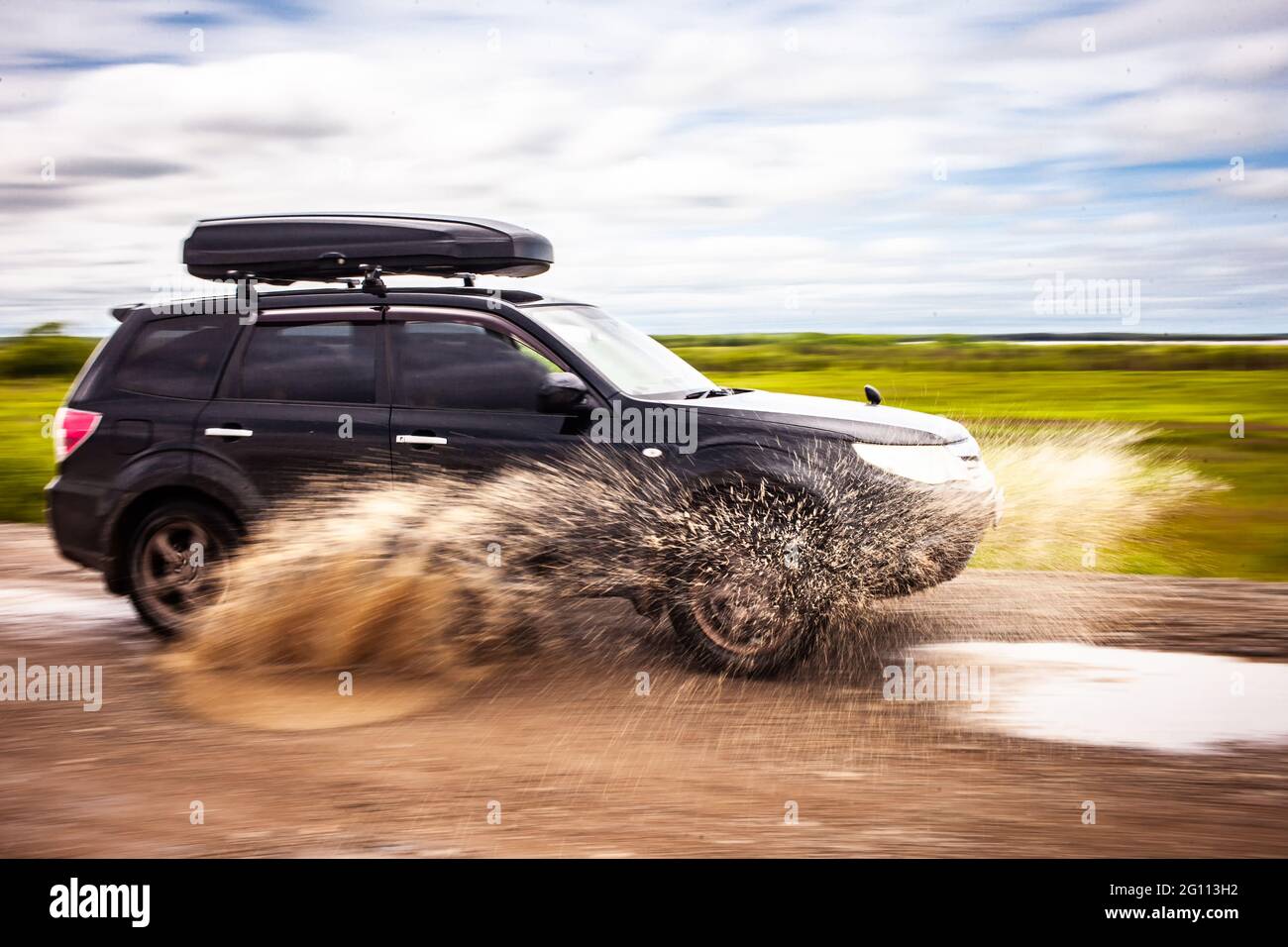 Schwarzer Subaru Forester fährt auf einer unbefestigten Straße mit Pfützen. Wasser spritzt unter den Rädern. Bewegungsunschärfe Stockfoto