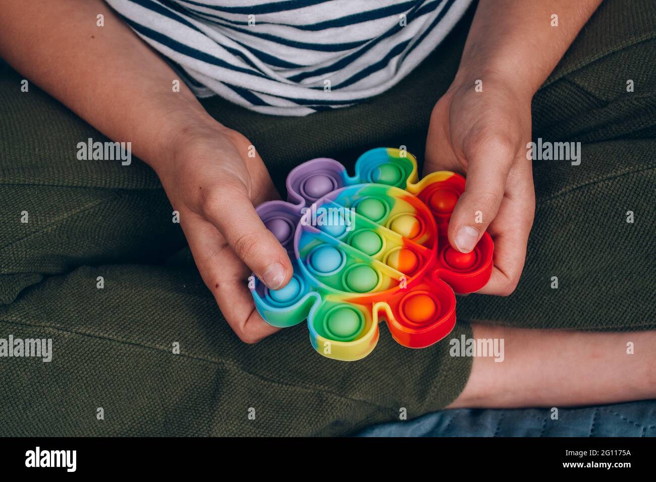 Nahaufnahme der Hände eines Jungen mit Regenbogen-Pop-it-Fidget-Spielzeug. Push Bubble Fidget Sensory Toy - waschbares und wiederverwendbares Silikon-Stressabbau-Spielzeug. Antistress Stockfoto