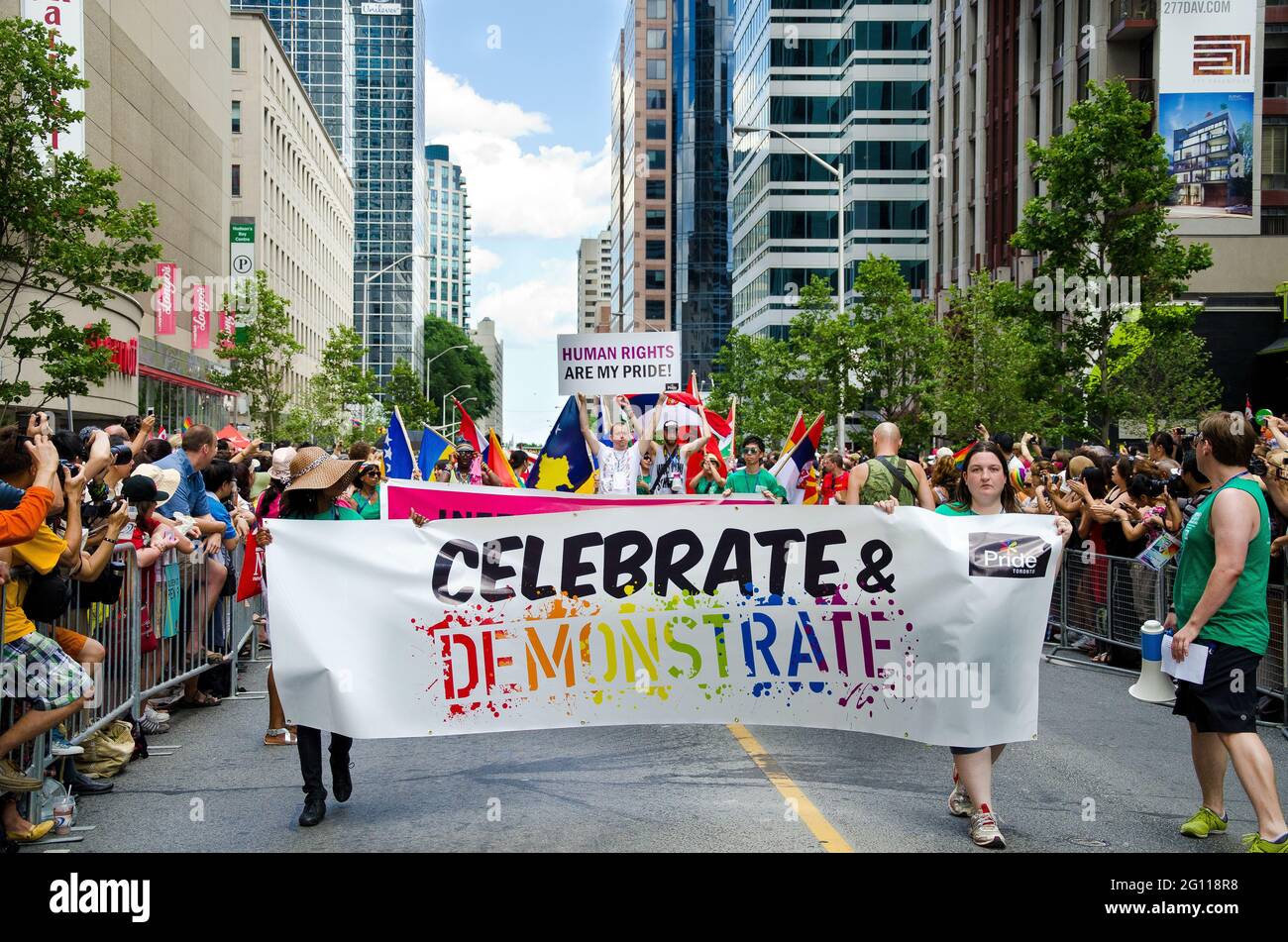 Marschieren Sie mit Fahnen und Transparenten bei der Pride Parade in Toronto durch die Straße, während die Zuschauermassen vom Rand aus jubeln Stockfoto