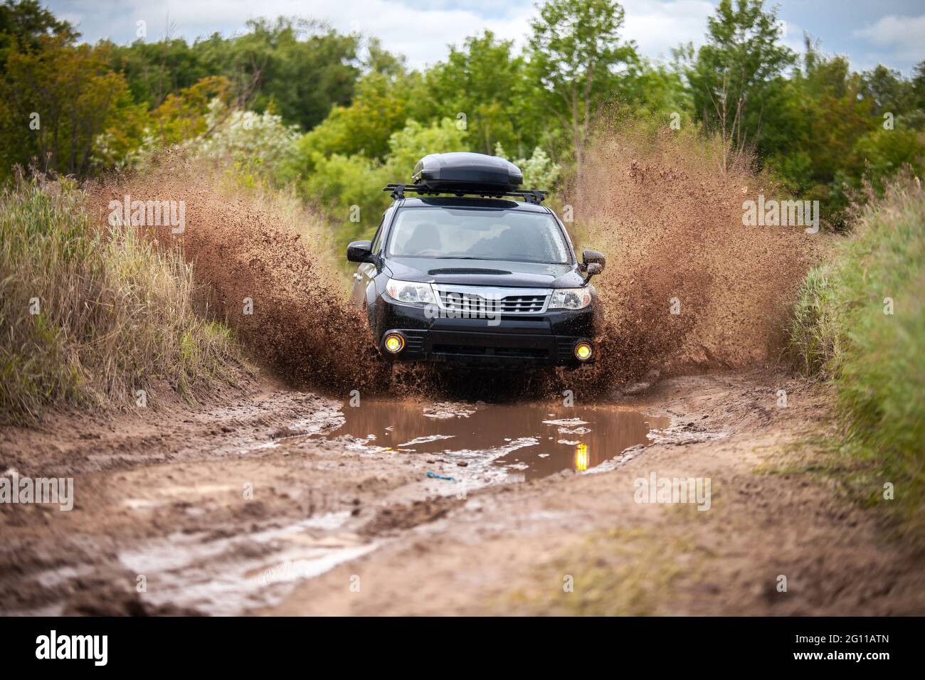 Schwarzer Subaru Forester, der sich auf einer schmutzigen Waldstraße bewegt und viel Wasser spritzt Stockfoto