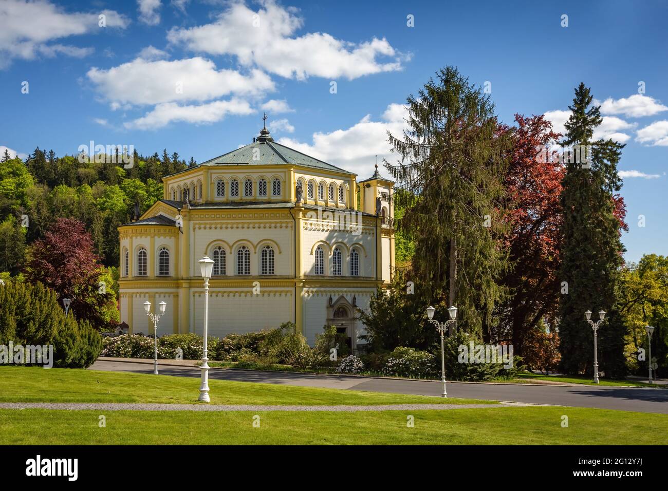 Marianske Lazne, Tschechische Republik - Mai 30 2021: Ansicht der christlichen Kirche Mariä Himmelfahrt vom Goetheplatz aus. Grüner Rasen und Bäume herum. Stockfoto