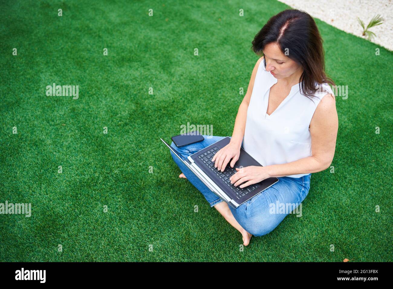 Eine kaukasische Brünette benutzt ihren Laptop im Garten ihres Hauses, es ist tagsüber Tageslicht Stockfoto