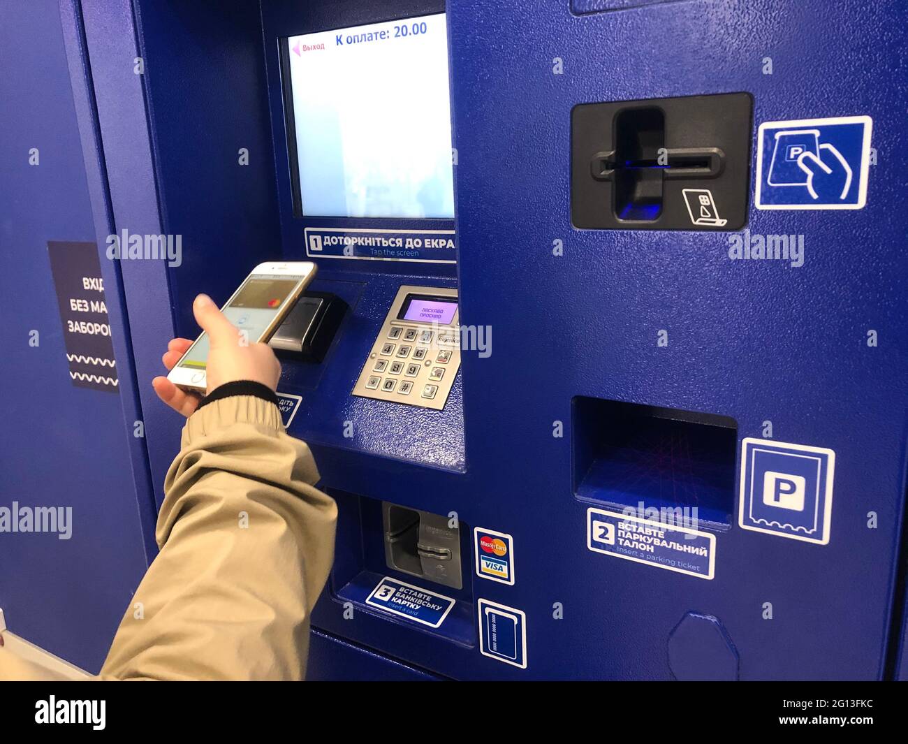 Ein Fahrer, der die Parkgebühr an der Bezahlstation zahlt, ein Geldautomat, ein kostenpflichtiger Parkplatz. Eine Person, die Terminal und Smartphone mit PayPass nutzt. Eine Hand, die ein Ticket in den Steckplatz einlegt Stockfoto