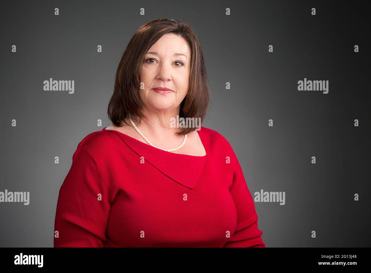 Eine leitende Frau in einem roten Pullover in einem ernsthaften Unternehmensporträt, horizontales Format auf grauem Hintergrund. Stockfoto