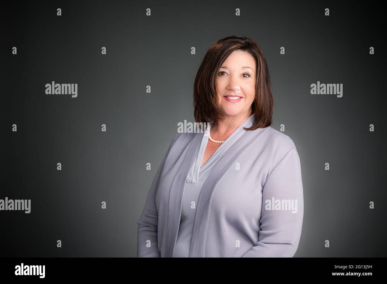 Eine lächelnde Frau in ihrem Firmenstudio – Porträt – Headshot. Grauer Hintergrund, horizontale Komposition. Glückliche Führungskraft. Stockfoto