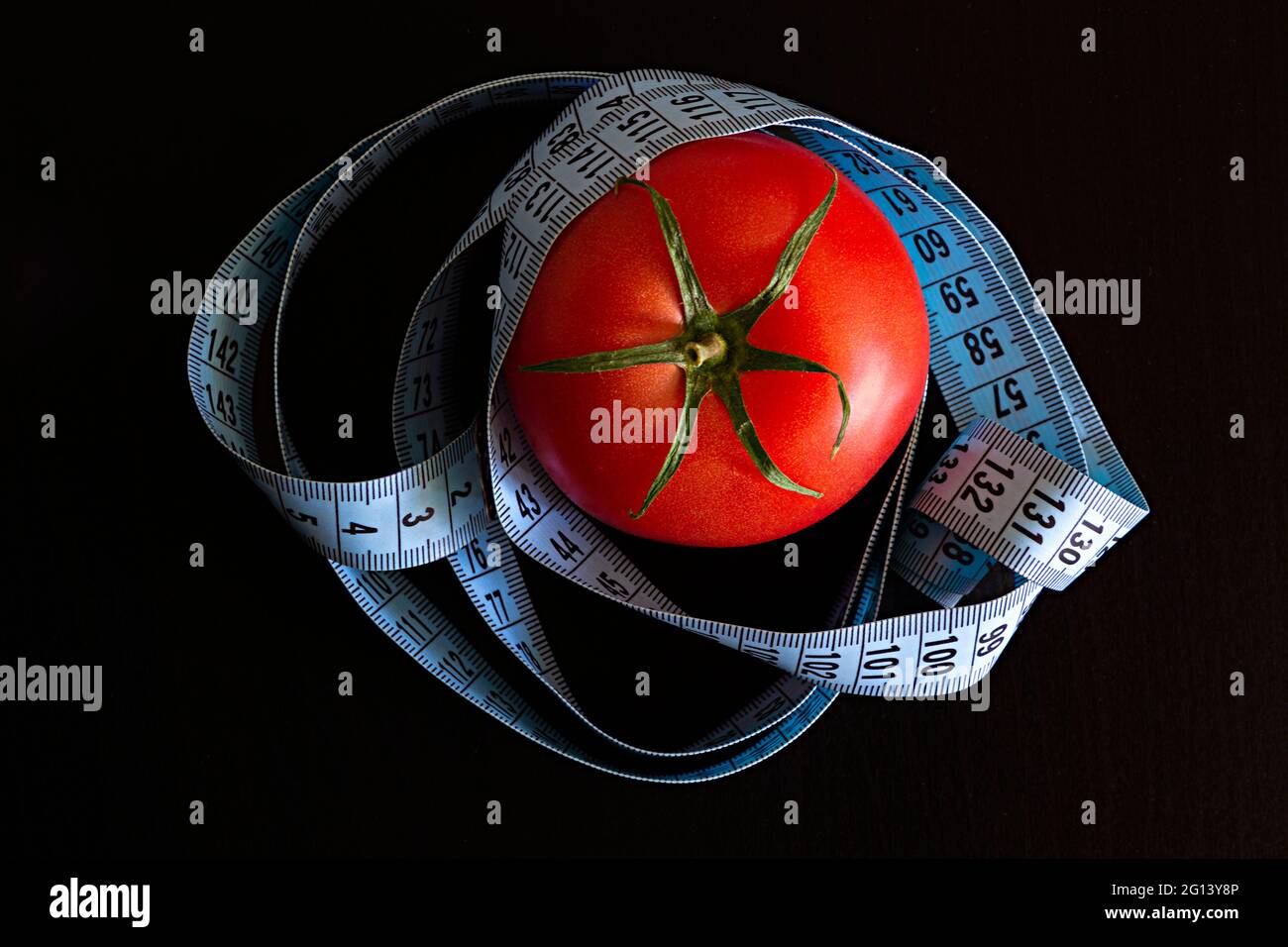 Tomate und ein blaues Meterband auf schwarzem Hintergrund, Konzept für gesunde Ernährung und Ernährung Stockfoto
