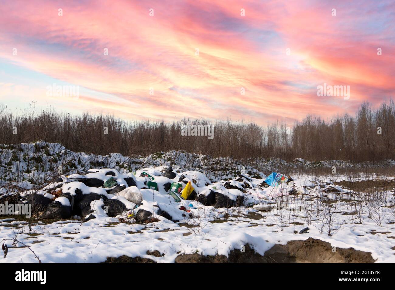 Ökologische Krise. Unterschiedlicher Müll und Müll auf Schnee am wunderschönen Winterwald am bunten Himmel. Umweltverschmutzung durch Müll. Destruktives Summen Stockfoto