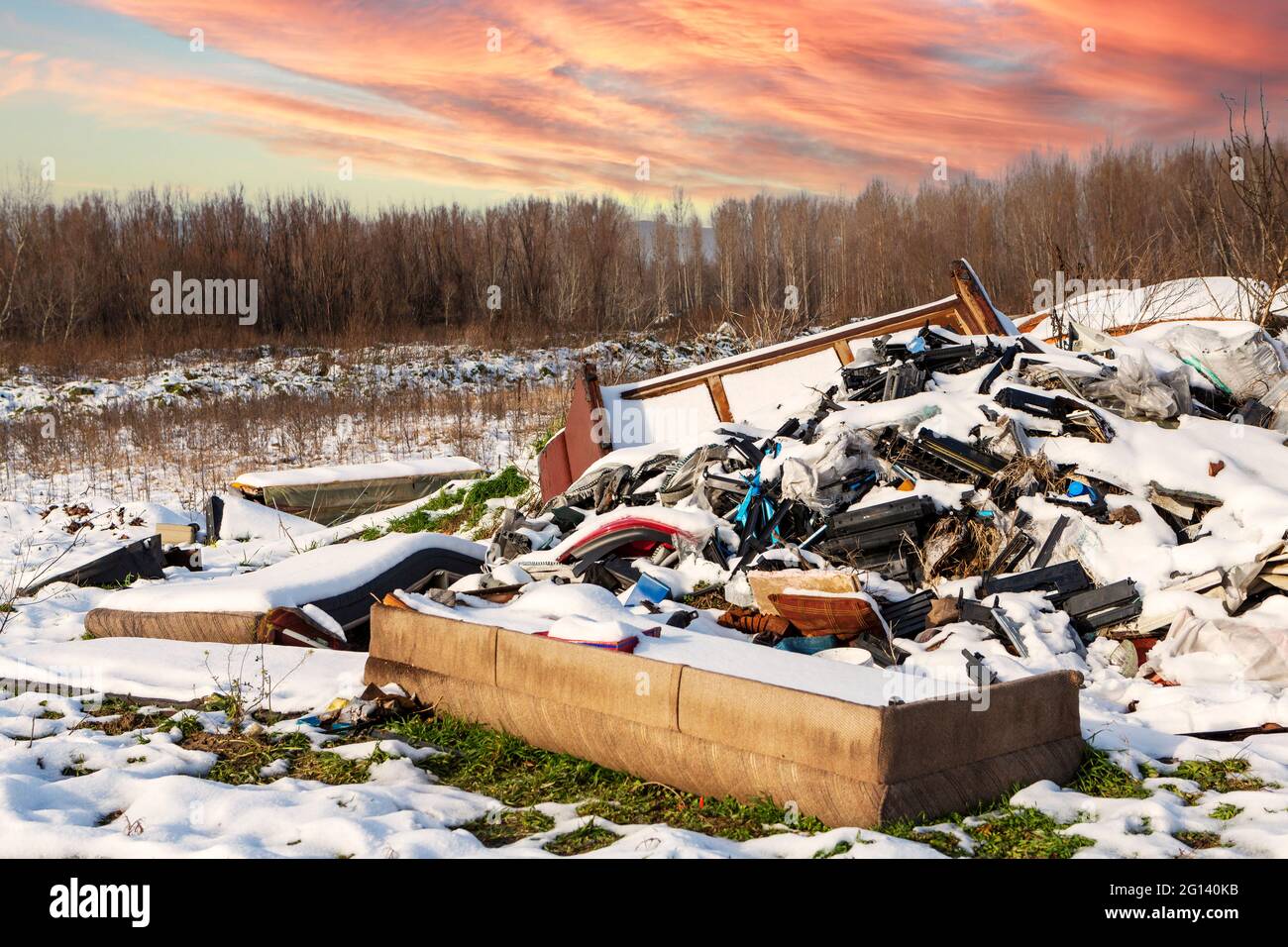 Ökologische Krise. Unterschiedlicher Müll und Müll auf Schnee am wunderschönen Winterwald am bunten Himmel. Umweltverschmutzung durch Müll. Destruktives Summen Stockfoto