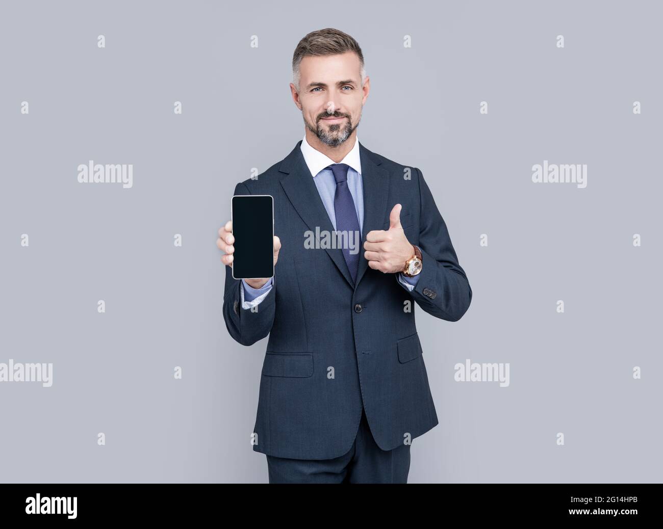 Reifer Mann Influencer in Anzug präsentiert Handy-Gerät und zeigen Daumen nach oben, beste Angebot. Stockfoto