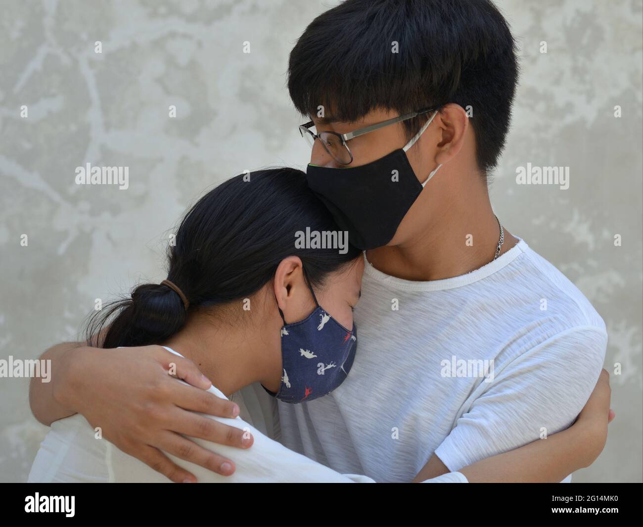 Während der globalen Coronavirus-Pandemie werden ein Paar junger Liebhaber mit dunklen Stoffmasken in eine zärtliche Umarmung gesperrt. Stockfoto