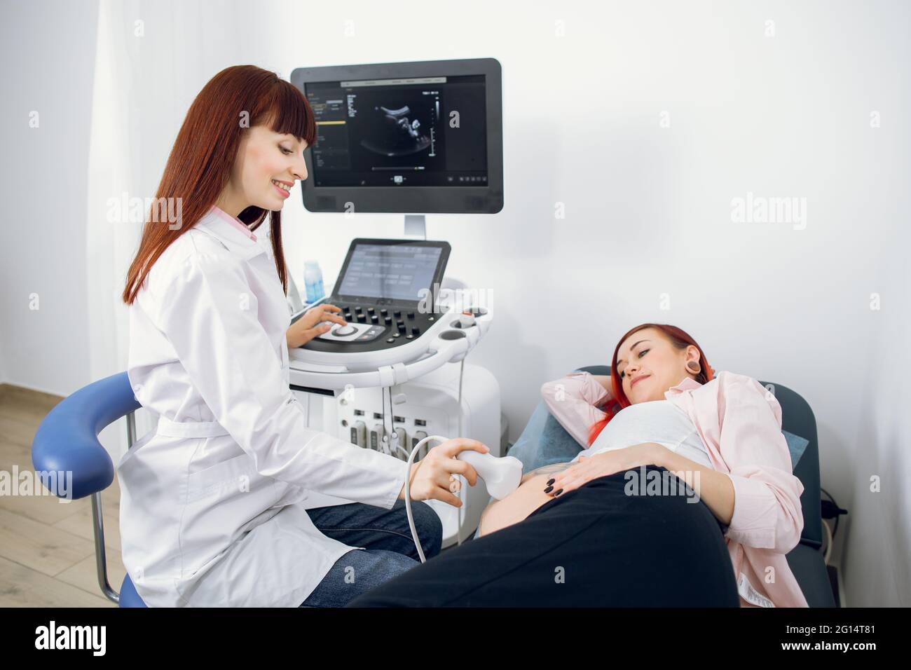 Weibliche glücklich lächelnde Doctor führt Ultraschall-Untersuchung ihrer weiblichen Patientin für die regelmäßige Screening der Schwangerschaft in der modernen medizinischen Büro Stockfoto