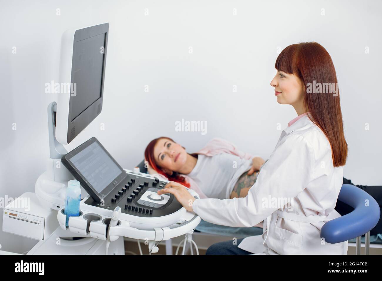 Porträt eines hochqualifizierten professionellen kaukasischen Geburtshelfers Arzt, der eine Schwangerin per Ultraschall untersucht. Schwanger Dame mit Ultraschall-Screening in der modernen medizinischen Klinik Stockfoto