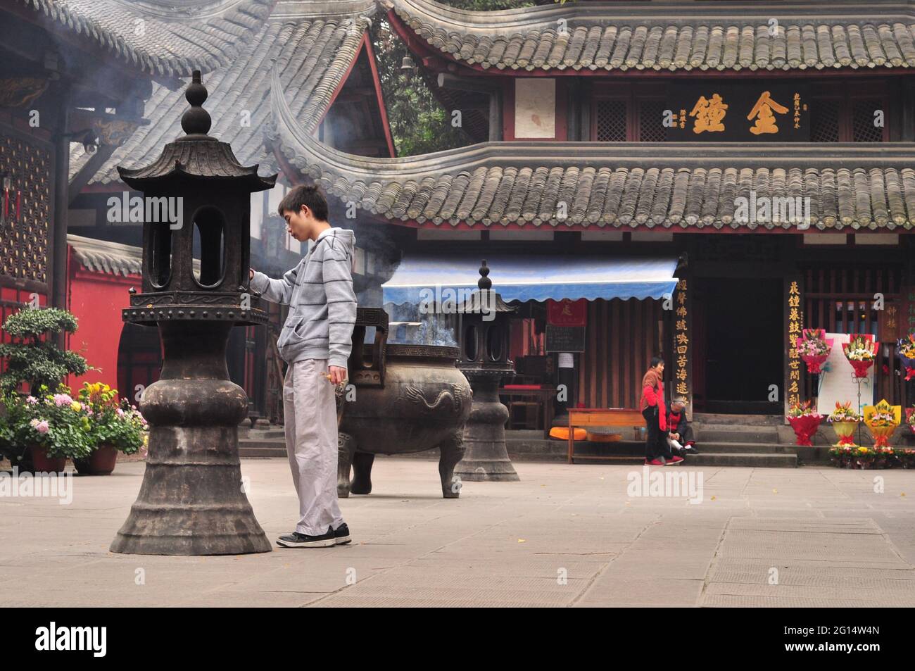 Ein junger Mann in einem chinesischen Tempel legt Weihrauch in eine spezielle Schüssel Stockfoto