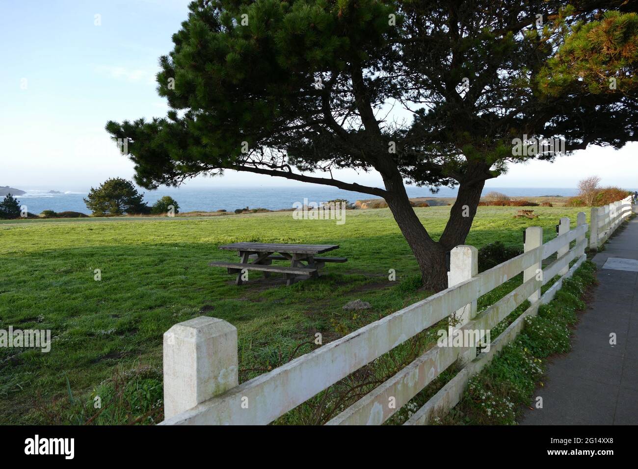 Picknicktisch auf einem grasbewachsenen Hügel hinter einem weißen Holzzaun Stockfoto