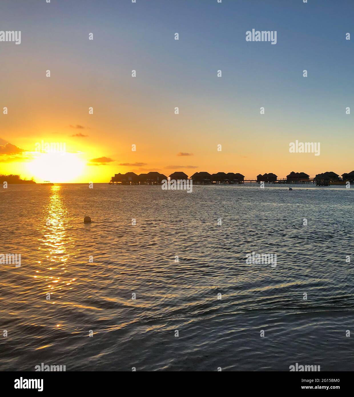 Sonnenuntergang über dem Ozean: Sonnenuntergang an Jamaikas Westküste mit über-dem-Wasser-Bungalows, die vor der erstaunlichen Sonne silhouettiert wurden Stockfoto