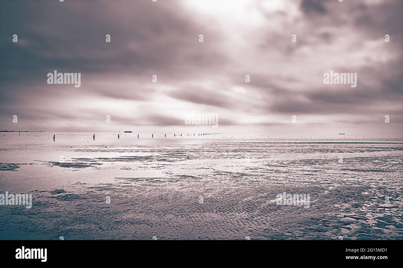 Surrealismus Wattenmeer Strand von Cuxhaven an der deutschen Nordseeküste. Sandstrand bei Ebbe mit Kugelbake, ein Seezeichen aus Holz an der Küste Stockfoto