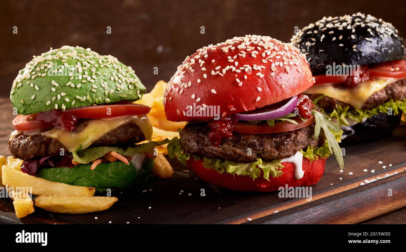 Appetitliche Hamburger mit bunten Brötchen und Fleischschnitzel, serviert auf dem Tisch mit Pommes frites Stockfoto