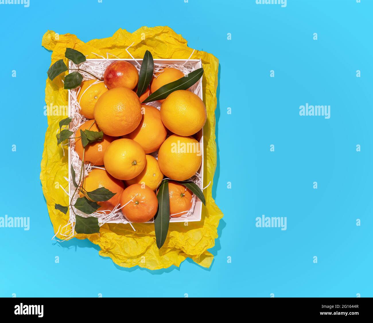 Horizontale, sommerliche Fruchtkomposition mit frischen Orangen in einer weißen Schachtel auf blauem Hintergrund mit Kopierraum. Gesund, würzen, landwirtschaftliche Lebensmittel Stockfoto