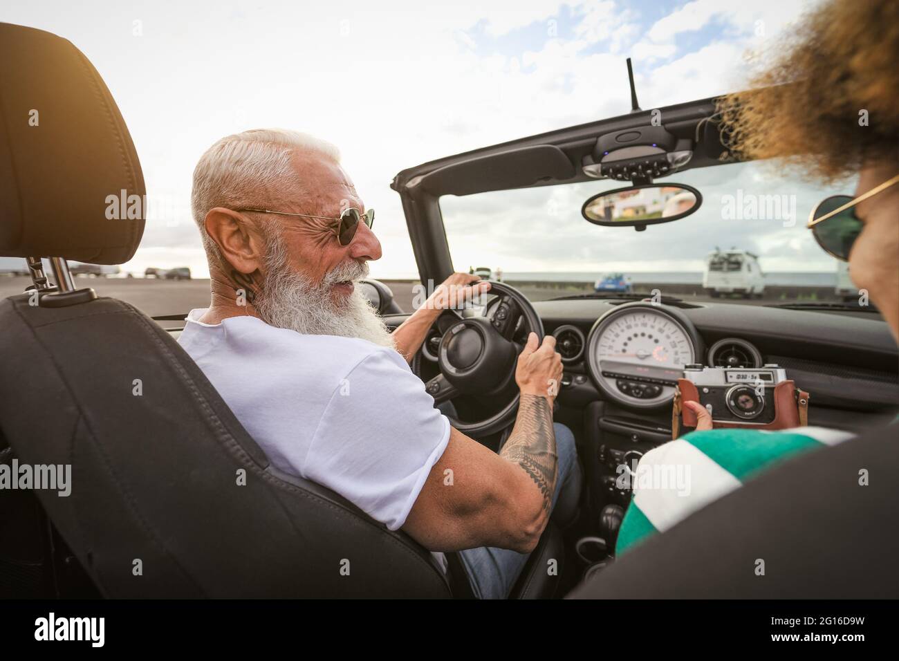 Glückliches Seniorenpaar, das Spaß hat, mit altem Vintage zu fotografieren Kamera während der Fahrt mit einem neuen Cabriolet während der Autofahrt Toururlaub Stockfoto Glückliches Seniorenpaar, das Spaß hat, mit altem Vintage zu fotografieren Kamera während der Fahrt mit einem neuen Cabriolet während der Autofahrt Toururlaub Stockfoto