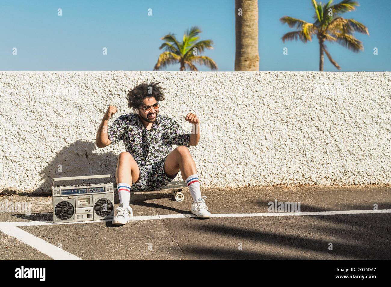 Junger afro-lateinischer Mann, der während der Sommerferien Spaß beim Tanzen hat, während er Musik mit Kopfhörern und Vintage-Boombox hört Stockfoto