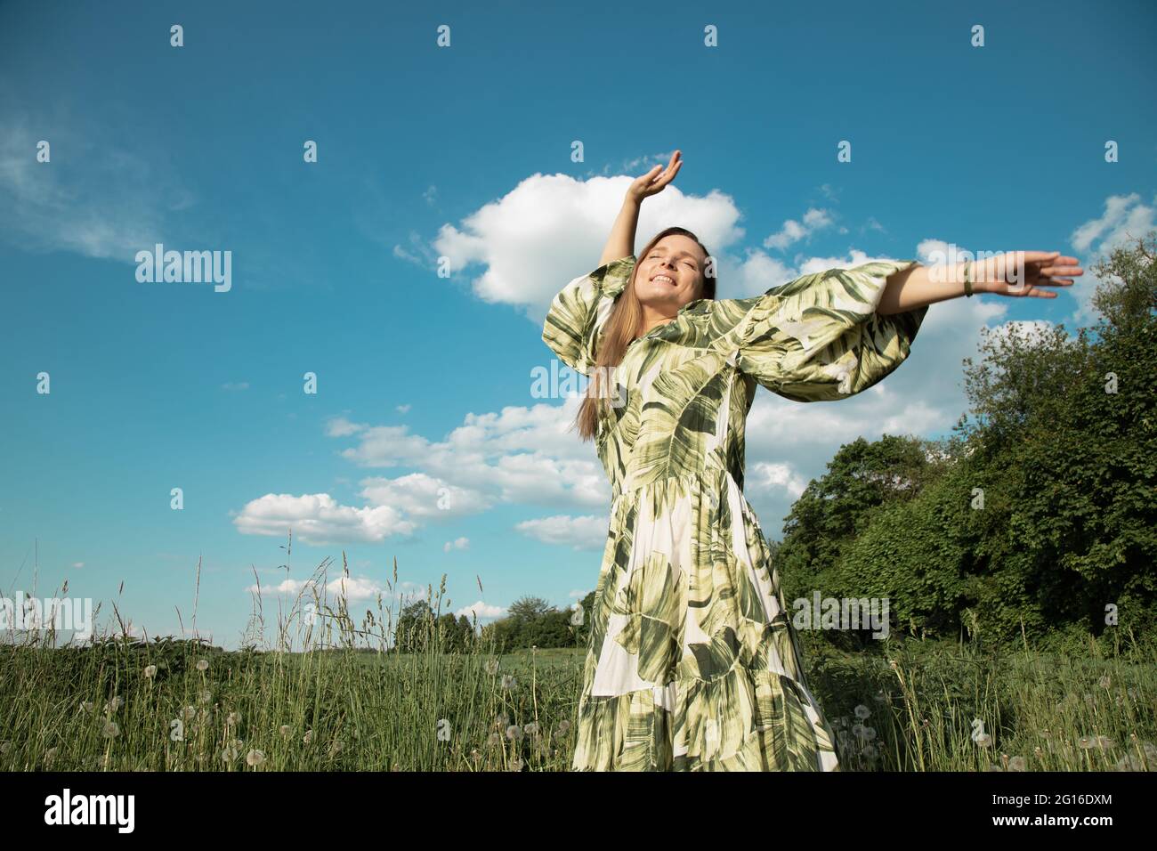 Junge Frau im grünen Feld mit ausgestreckten Händen zum blauen Himmel, Glück Stockfoto