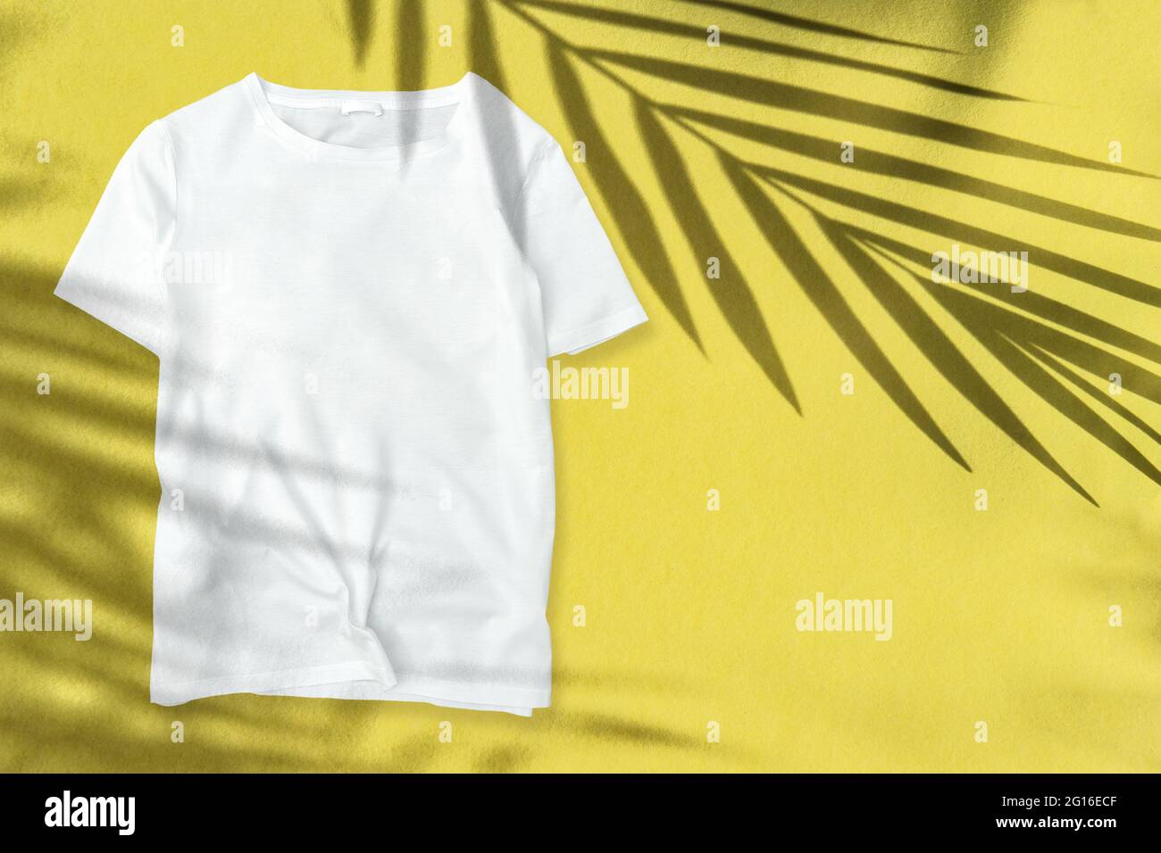Sommervorlage mit T-Shirt-Mockup mit Blumenmuster. Handfläche hinterlässt Schatten auf gelbem Hintergrund Stockfoto