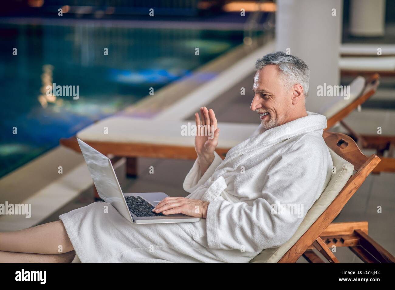 Ein grauhaariger bärtiger Mann in einem weißen Bademantel, der Zeit im Internet verbringt Stockfoto