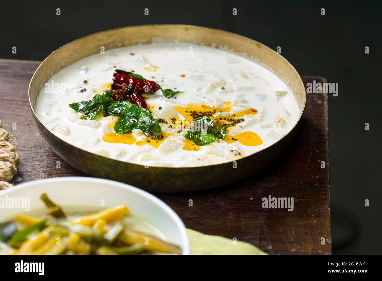 Pachadi oder Raitha und olan Kerala Festmahlgerichte, vegetarische Gerichte in einem Messinggefäß und einer weißen Schale, die auf einem Holzboden platziert ist Stockfoto