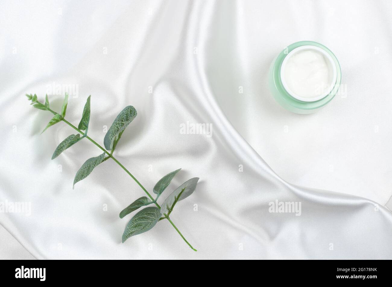 Bio-Kosmetik für die Hautpflege. Ein Glas Creme und ein Zweig Eukalyptus auf seidenem Hintergrund. Stockfoto