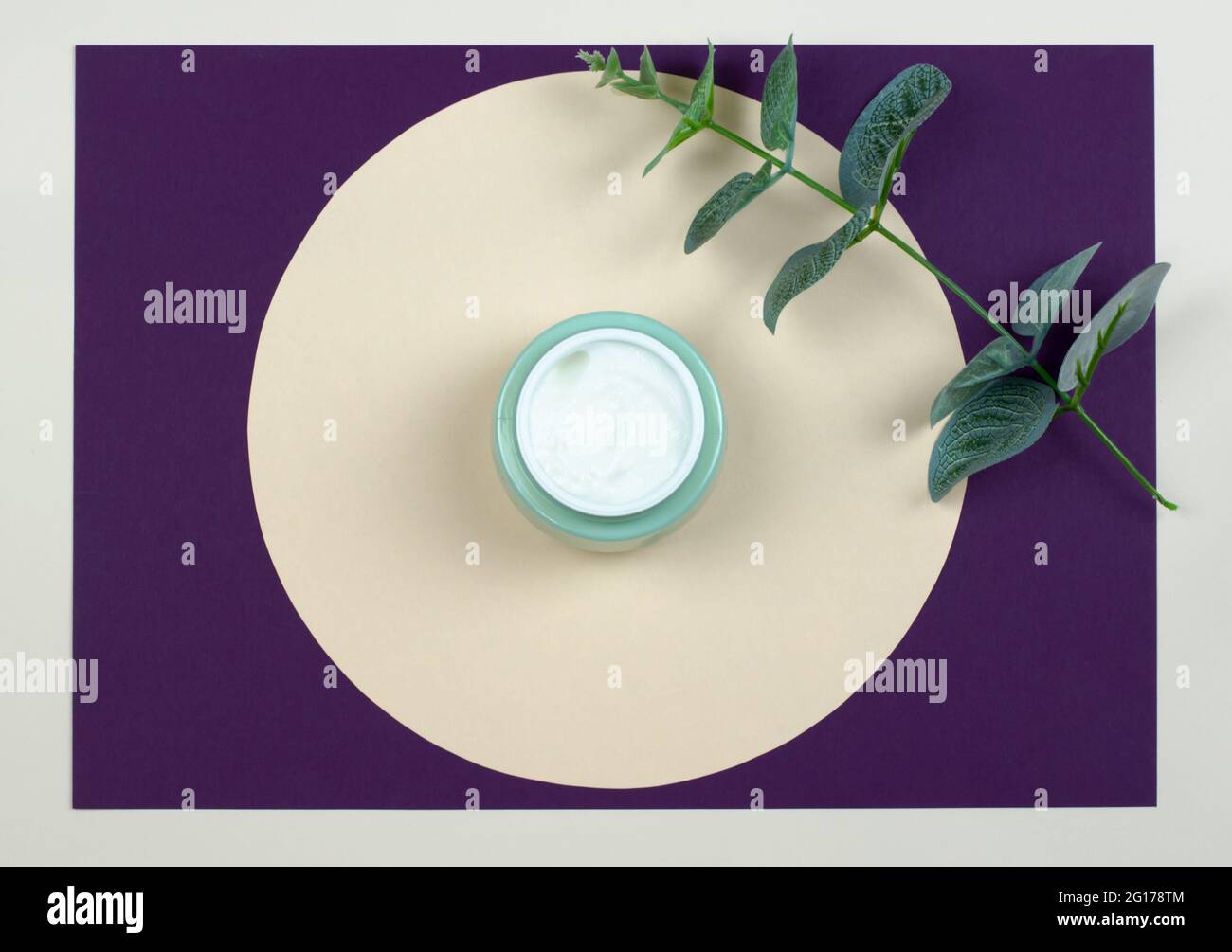 Draufsicht auf ein offenes Glas mit cremefarbenen und grünen Blättern auf farbigem Hintergrund. Beauty-Konzept mit kosmetischen Produkten für das Gesicht. Stockfoto