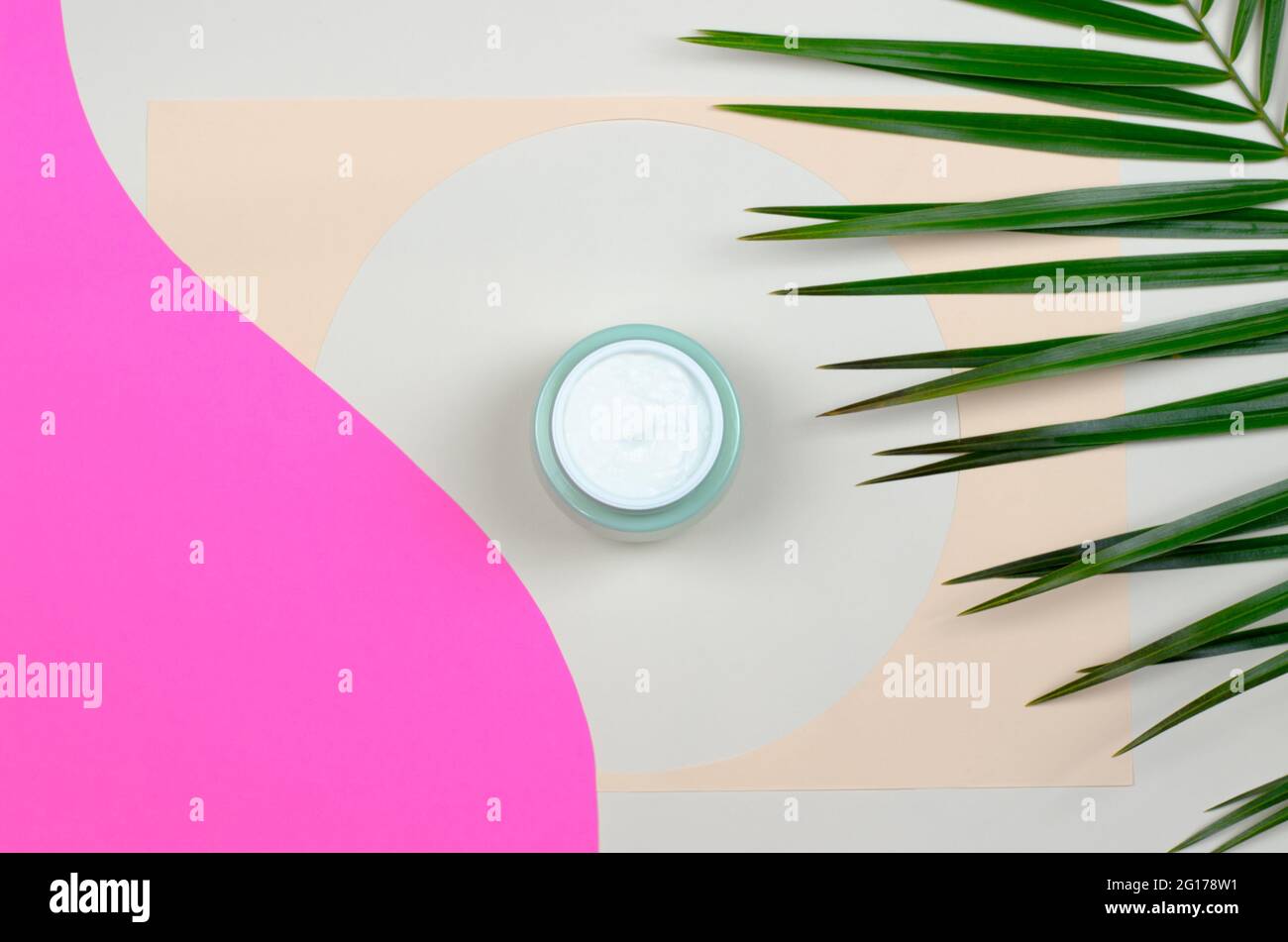 Draufsicht auf ein offenes Glas mit cremefarbenen und grünen Blättern auf farbigem Hintergrund. Beauty-Konzept mit kosmetischen Produkten für das Gesicht. Stockfoto