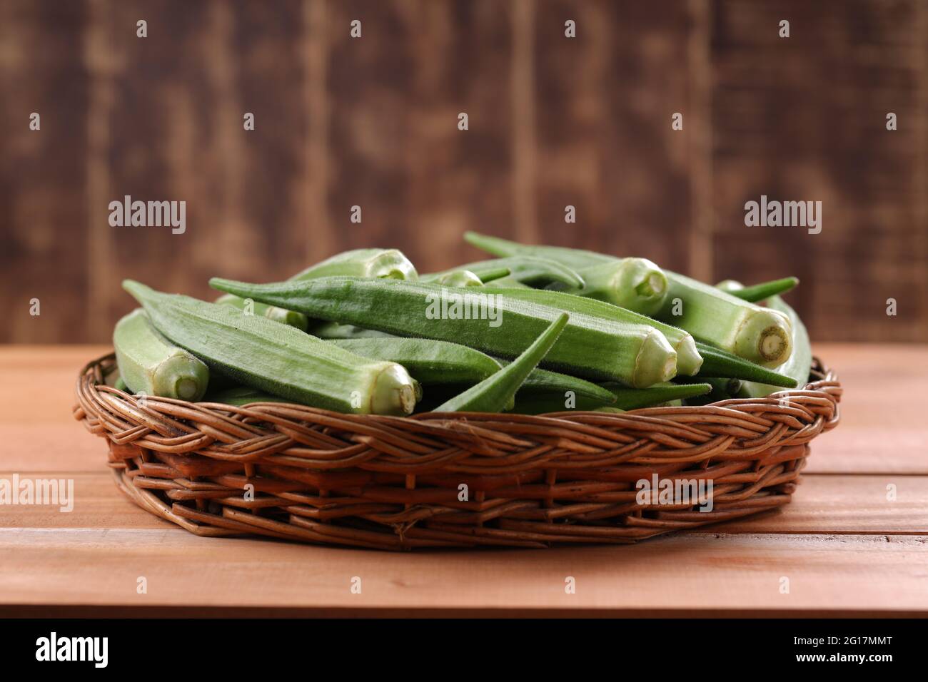 Okra oder Lady's Finger oder Bhindi frisches grünes Gemüse in einem Korb mit Holzstruktur Hintergrund angeordnet, isoliert und selektive Fokus Stockfoto