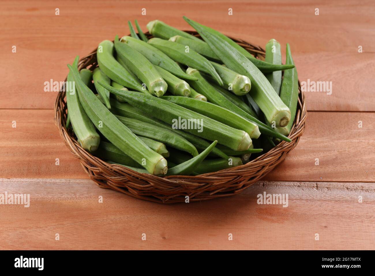 Okra oder Lady's Finger oder Bhindi frisches grünes Gemüse in einem Korb mit Holzstruktur Hintergrund angeordnet, isoliert und selektive Fokus Stockfoto