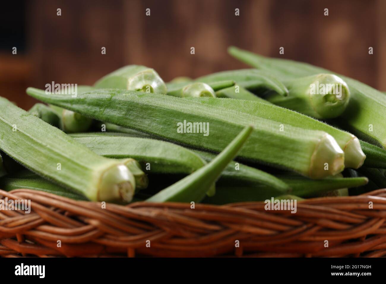 Okra oder Lady's Finger oder Bhindi frisches grünes Gemüse in einem Korb mit Holzstruktur Hintergrund angeordnet, isoliert und selektive Fokus Stockfoto