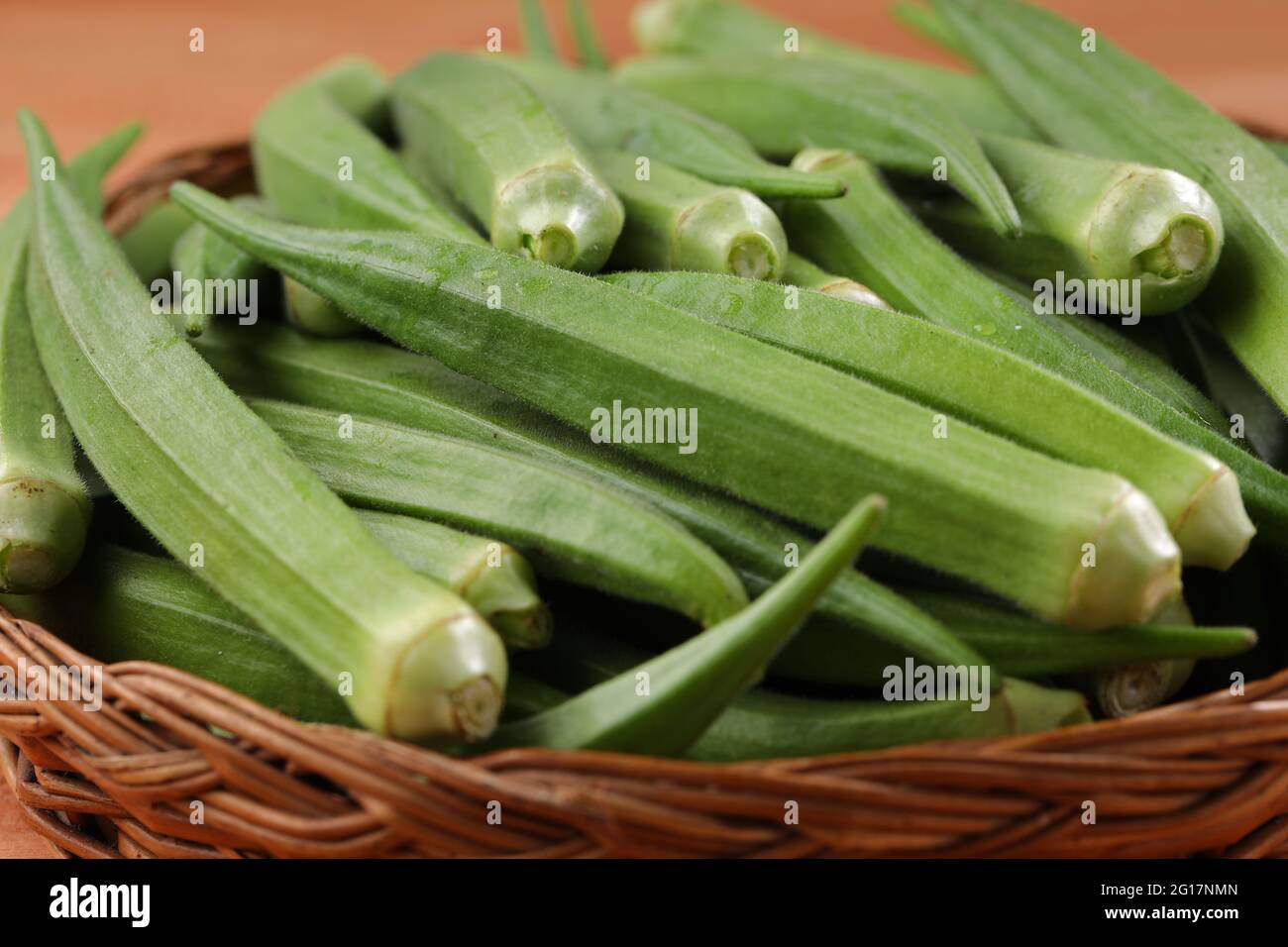 Okra oder Lady's Finger oder Bhindi frisches grünes Gemüse in einem Korb mit Holzstruktur Hintergrund angeordnet, isoliert und selektive Fokus Stockfoto