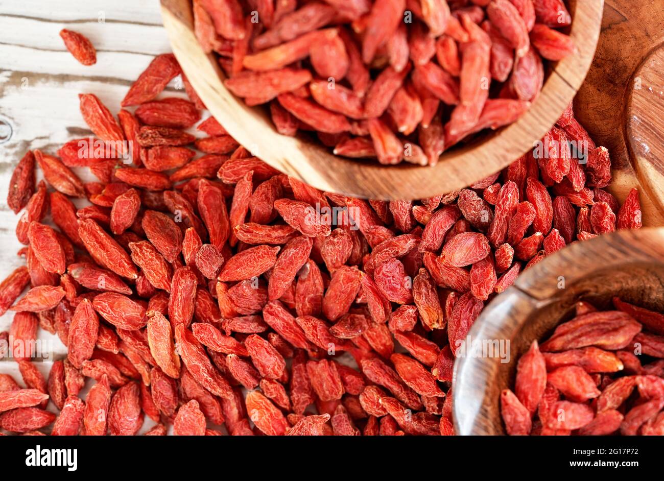 Getrocknete Goji-Beeren in Holzschüsseln, mehr verstreut über weiße Bretter Tisch unter, Nahaufnahme Detail von oben Stockfoto