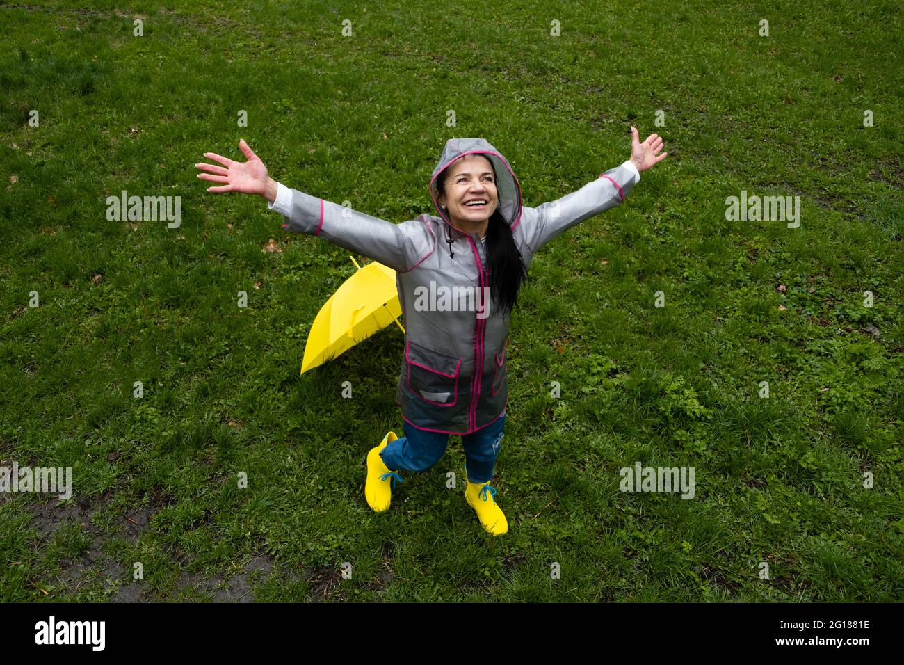 Glückliche ältere Frau, fröhliche ältere, ältere, pensionierte Frau mit gelbem Regenschirm, die das Leben an regnerischen Tagen im Park genießt. Genießen Sie jeden Moment, genießen Sie das Leben Stockfoto