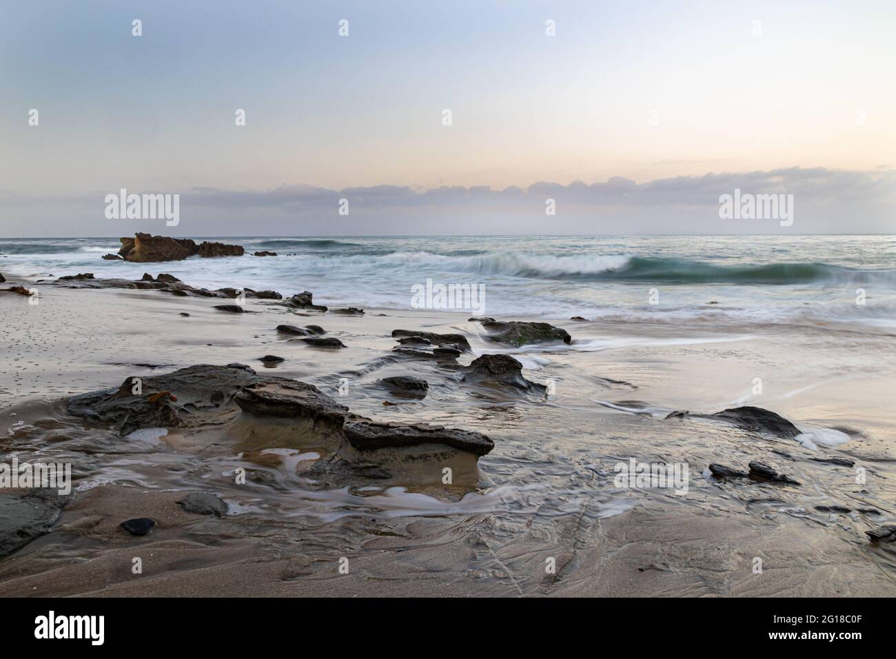 Verwitterte Felsen im Sand in Laguna Beach, Kalifornien. Wellen und mehr Felsen vor der Küste. Am frühen Morgen Himmel mit Wolken in der Ferne. Stockfoto