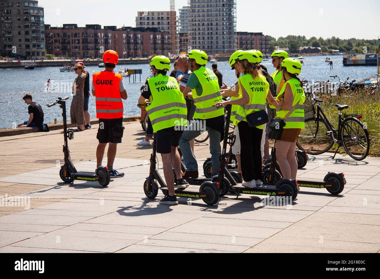 Eine Gruppe junger Menschen, die auf einer geführten Sightseeing-Tour mit Motorroller unterwegs sind, hält an einem Stadthafen in sonniger Sonne, sieht nach, reist und hält an Gebäuden. Kopenhagen, D Stockfoto