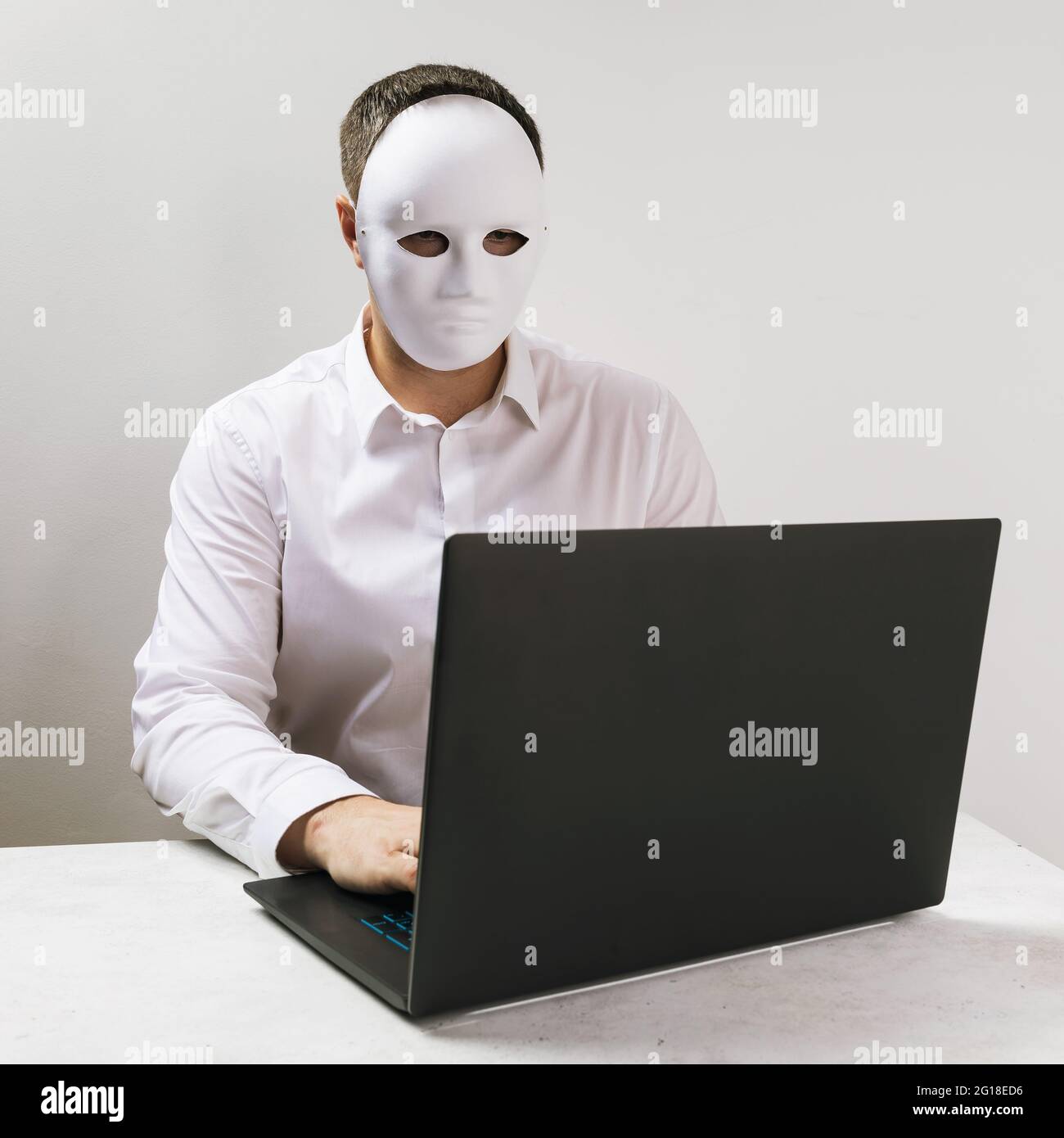 Ein Mann in einer Maske arbeitet hinter einem Laptop, dem Begriff der Anonymität im Internet. Stockfoto