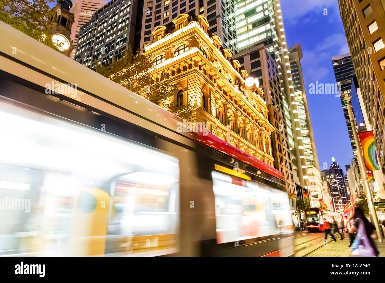 Die verschwommene Personenbahn entlang der George Street in der Innenstadt von Sydney überquert bei Sonnenuntergang den Martin Place - helle Lichter. Stockfoto