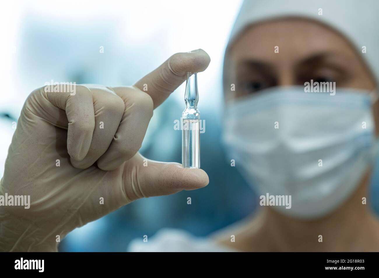 Der Arzt schaut auf die medizinische Ampulle in seiner Hand. Stockfoto