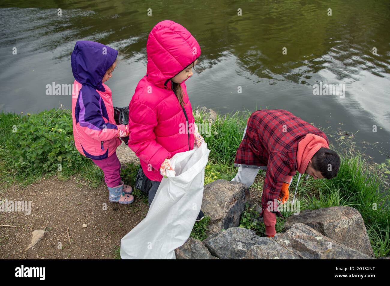 Kinder und Vater säubern Müll im Wald in der Nähe des Flusses. Stockfoto