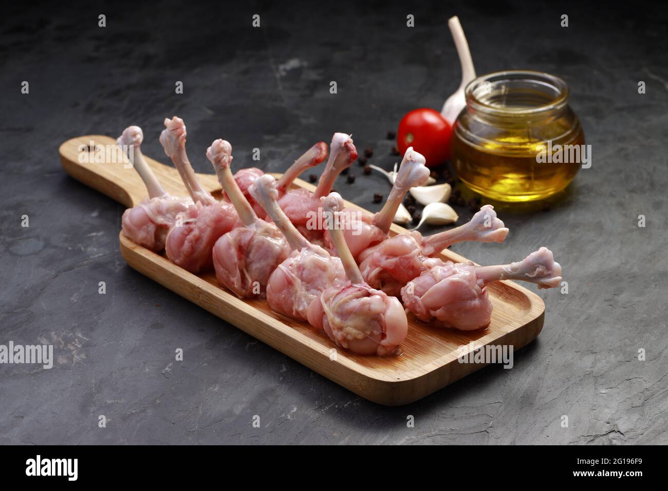 Roher Hühnerlollipop, zehn Stücke Hühnerlollipop auf einem Servierbrett mit Öl, Tomate und Knoblauch auf dem Hintergrund mit grauer strukturierter Basis angeordnet Stockfoto