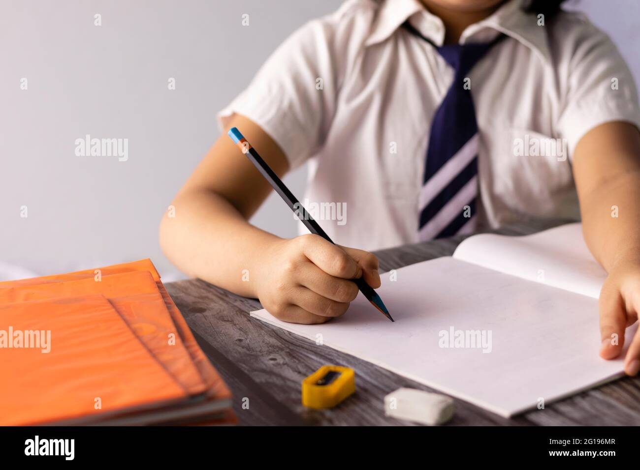 Selektiver Fokus auf die Hand eines indischen Kindes, das mit schreibt Bleistift auf dem Notizbuch in Schuluniform Stockfoto