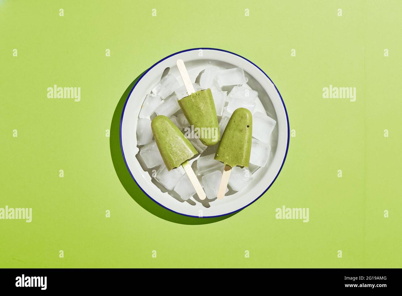 Gefrorener hausgemachter Pistazien-Popsicle in einer Schüssel mit Eis auf grünem Hintergrund. Erfrischender Fruchteis, gefrorener grüner Saft auf Stick. Draufsicht, Kopierbereich. Stockfoto