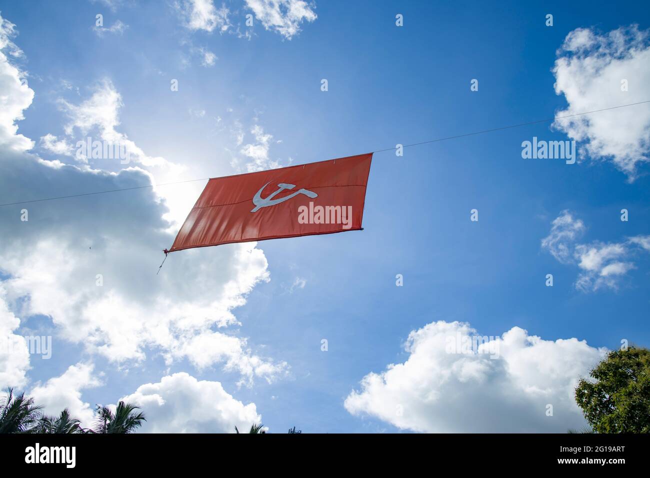 kommunistische Flagge. Hammer und Sichel, die die Bauern und die Arbeiter darstellen, fliegen im dichten, wolkigen blauen Himmel. Stockfoto