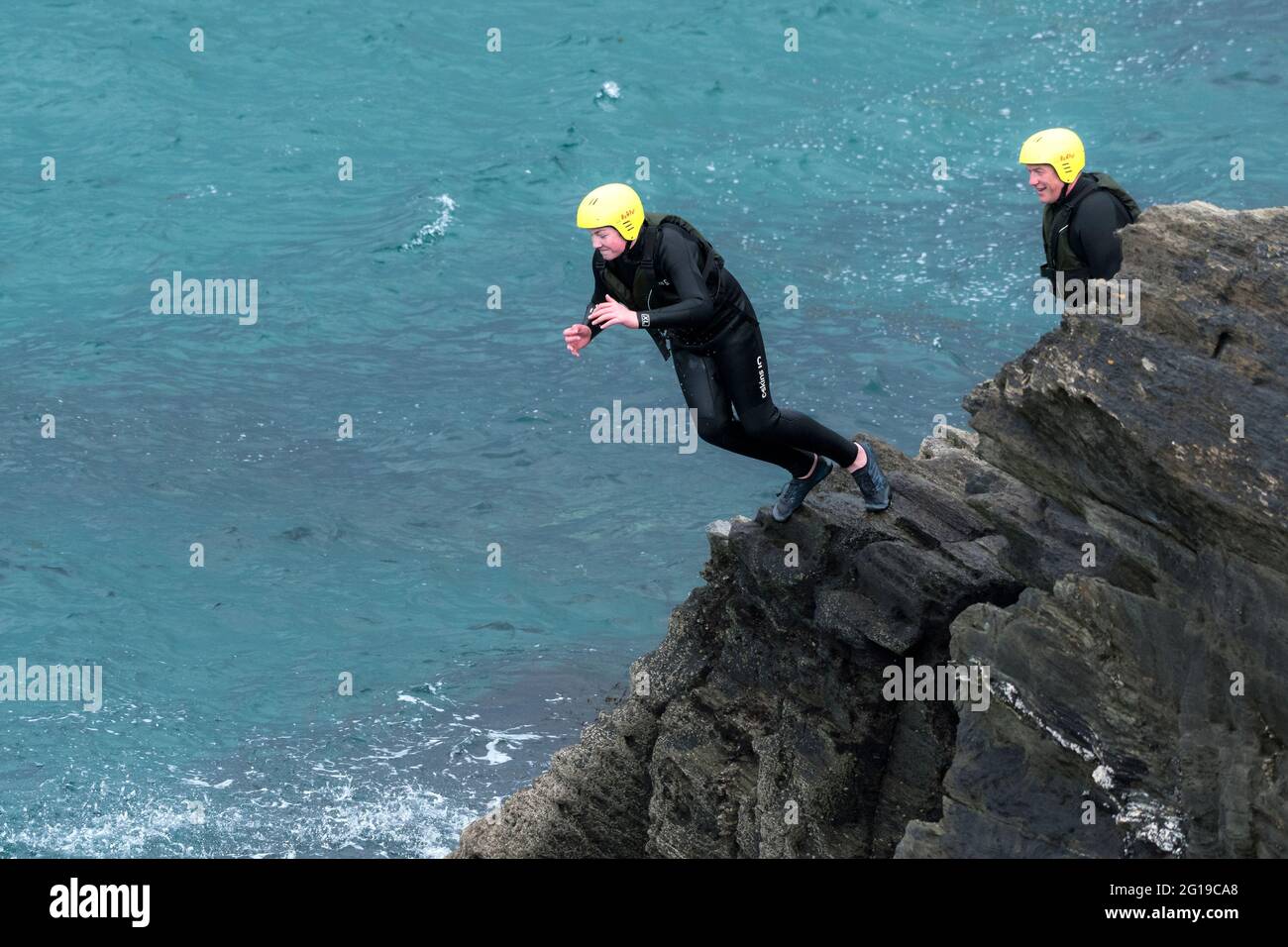 Ein junger Urlauber, der von Felsen ins Meer springt, auf einer Fahrt um Towan Head in Newquay in Cornwall. Stockfoto